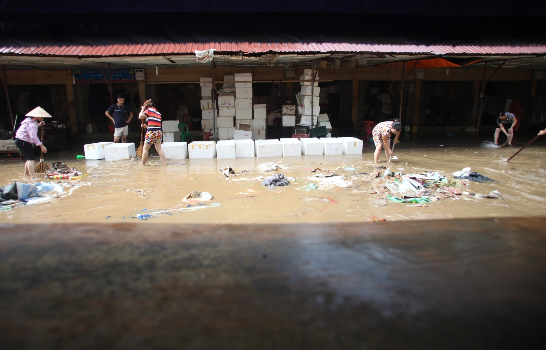 9.	Qua tấm bạt của dãy hàng thịt là gian hàng hoa quả cũng chịu chung số phận ngập lụt, bên cạnh là rác thải từ quanh đó ùn ùn kéo về.