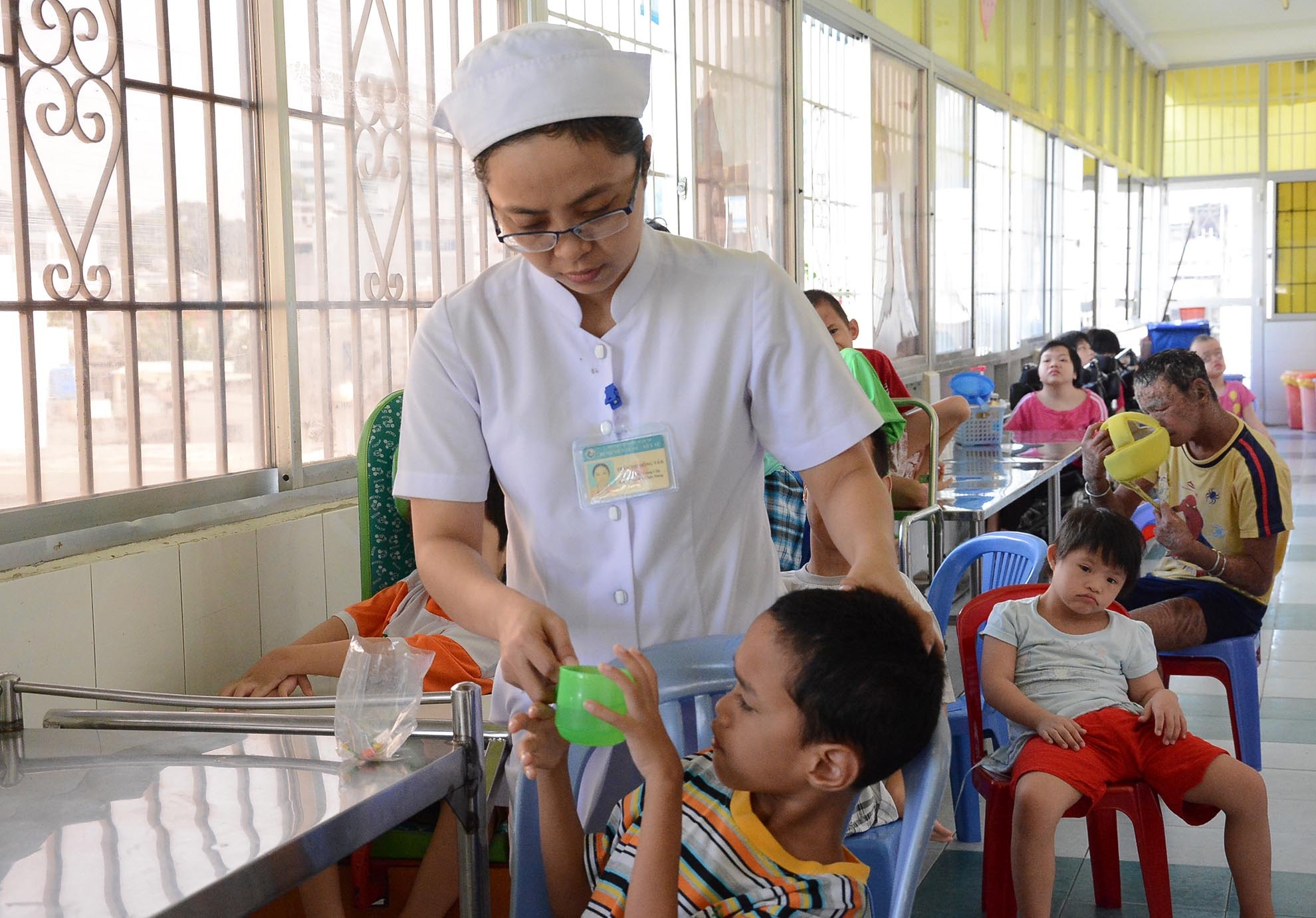 Làng Hòa Bình có 39 cán bộ, nhân viên thì có 36 người là nữ. Những nhân viên ở đây cùng với bà Chung vừa chăm lo việc ăn uống, chăm sóc sức khỏe, tập trị liệu, dạy chữ cho các em. Trong ảnh: Điều dưỡng Trần Thị Hồng Vân, hằng ngày thực hiện việc chăm sóc cho các em tại làng Hòa Bình.  