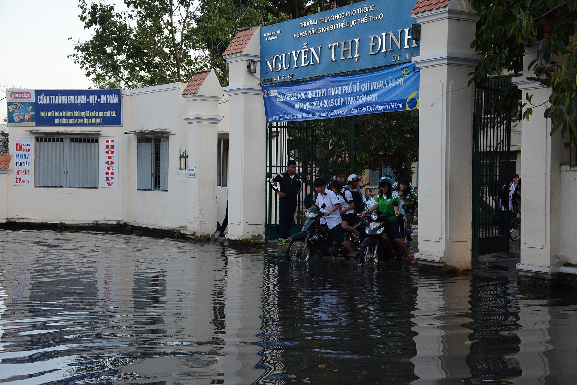Nước ngập trước cổng trường THPT Nguyễn Thị Định khiến các em học sinh đi lại khó khăn, một số học sinh còn chờ phụ huynh đến đón.