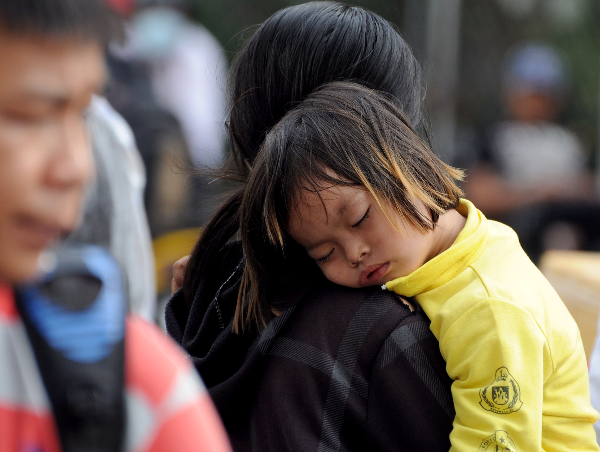 Một em bé ngủ trên lưng mẹ khi chờ đợi mua vé xem đội tuyển Olympic thi đấu.