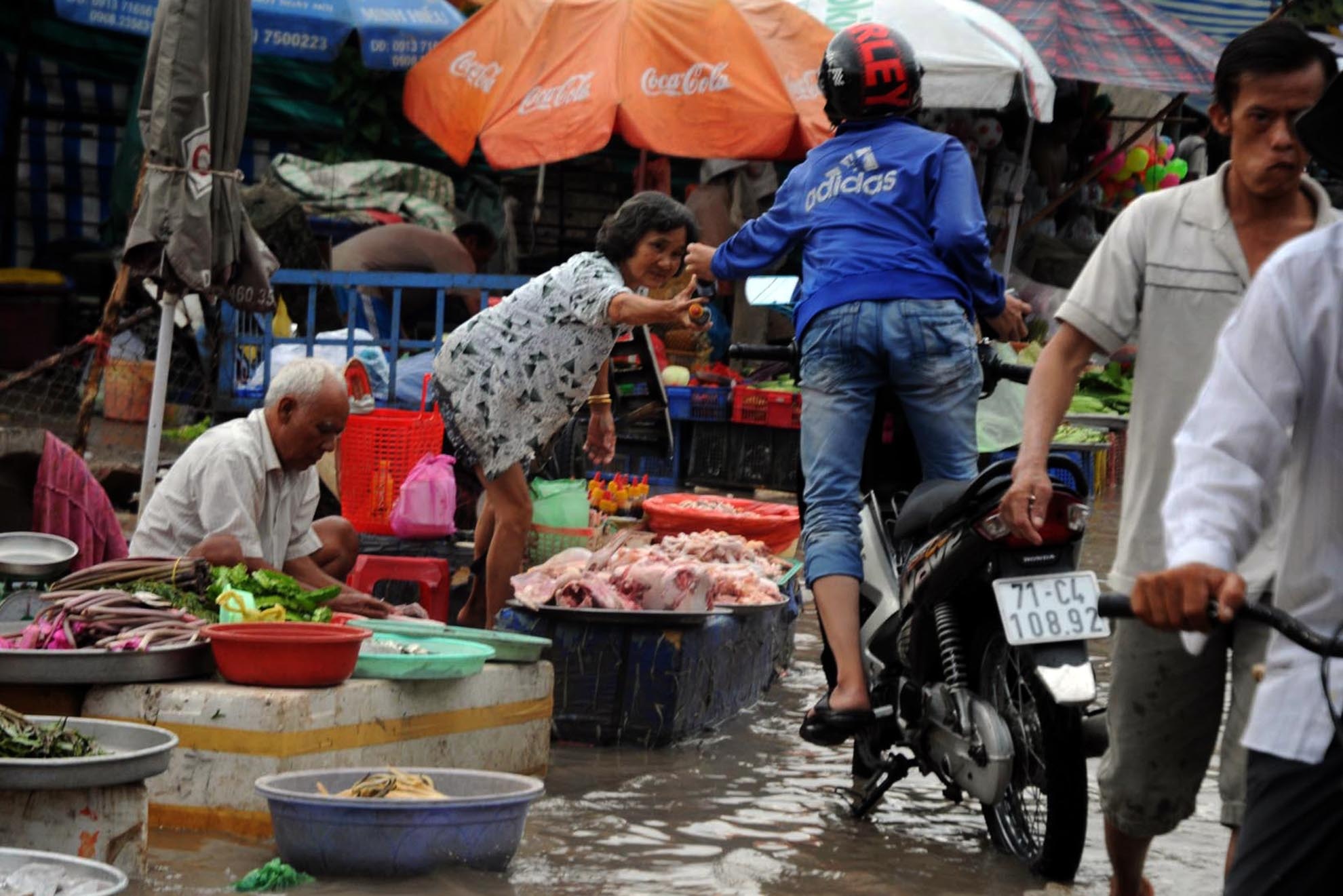Mưa lớn ngập đường, các tiểu thương ở  chợ trên đường An Dương Vương (quận Bình Tân) phải kê cao sạp ngồi buôn bán. Người dân đi làm về cũng phải bì bõm lội trong biển nước để mua thức ăn.