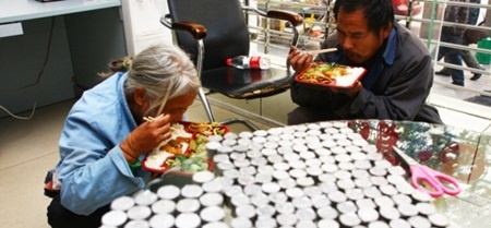 Đôi vợ chồng tranh thủ ăn trưa trong lúc đợi nhân viên ngân hàng đếm tiền xu.