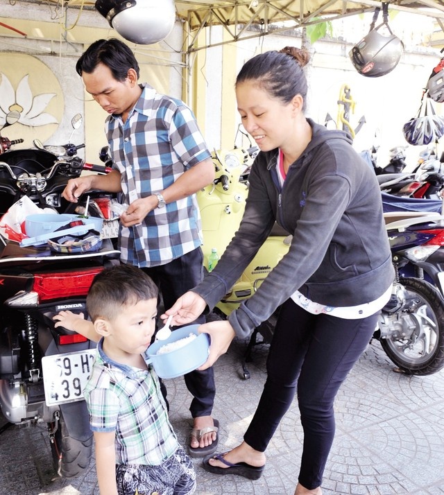 Cả nhà Tài “nhặt vợ” đang quây quần cơm trưa nơi bãi giữ xe. Bé Khang rất vui khi được ra bãi phụ ba Tài. 