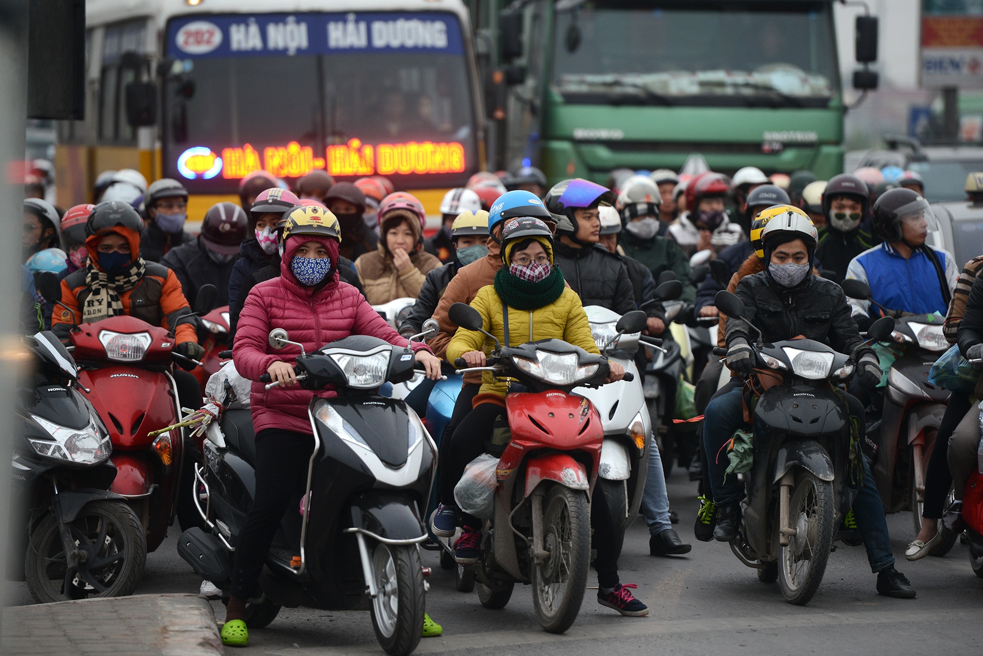 Cảnh người đi xe máy chôn chân chờ đèn đỏ cùng xe tải xe khách tại nút giao. 