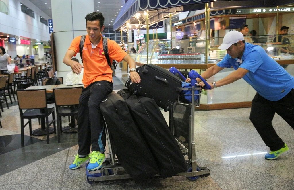 Văn Quyết và HLV thủ môn Nguyễn Đức Cảnh vui đùa với xe chở hành lý tại sân bay. 