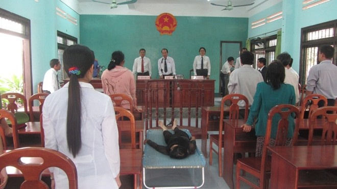 Bị cáo nằm giường nghe tòa xét xử.