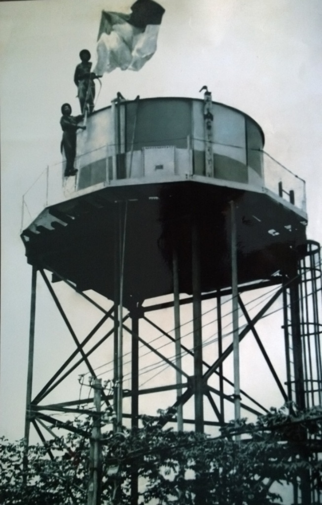 Ông Cẩn (người đứng dưới) cùng đồng đội cắm cờ giải phóng ở tháp nước sân bay Tân Sơn Nhất. Ảnh: NVCC.