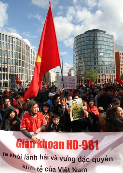 Nhiều người mặc áo dài truyền thống hoặc áo in hình cờ đỏ sao vàng, trên tay cầm cờ Tổ quốc, ảnh Bác Hồ, ảnh Đại tướng Võ Nguyên Giáp…cùng các băng rôn, khẩu hiệu viết bằng tiếng Việt, tiếng Anh và tiếng Đức.