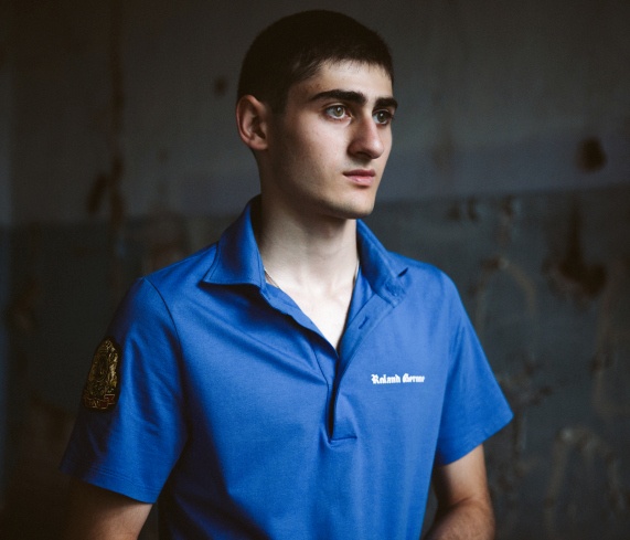 Alex Badoyev, 17 tuổi, đứng giữa căn phòng, nơi các tay súng đã bắn chết cha của em. Badoyev và cha mẹ nằm trong số 1.100 con tin.  Những kẻ khủng bố đe dọa chúng sẽ làm nổ tung trường học nếu cảnh sát cố gắng tiếp cận vào bên trong tòa nhà. Chúng đặt các em học sinh lên trên cửa sổ như lá chắn sống và nói rằng, chúng sẽ giết 50 con tin nếu một thành viên của nhóm mất mạng và 20 con tin cho mỗi kẻ bị thương. 