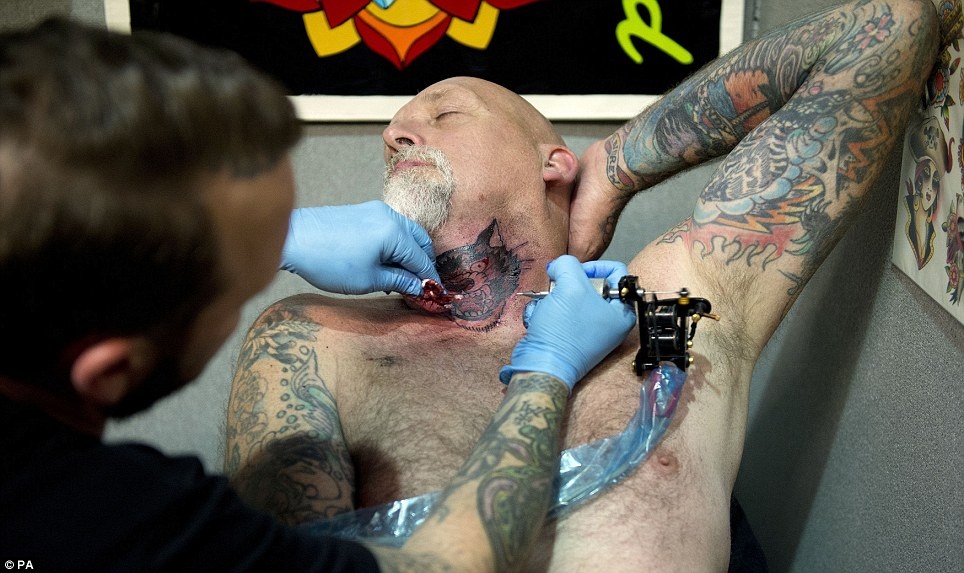 Một nghệ sĩ xăm hình cho du khách tại phần cổ họng. Ảnh: PA