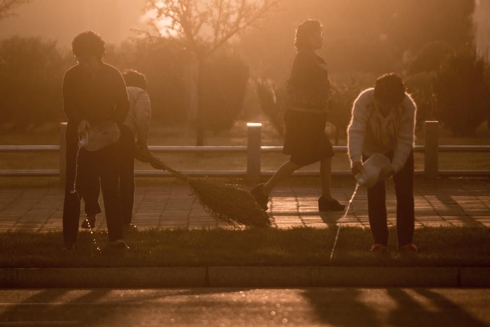 3 người phụ nữ tưới cây và quét dọn trên một con đường dưới ánh bình minh.