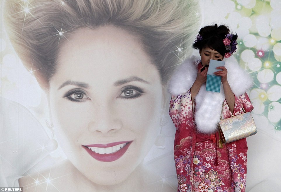 Một cô gái đứng trước một tấm biển quảng cáo để trang điểm trước khi đến công viên tại Tokyo dự lễ trưởng thành. Ảnh: Reuters