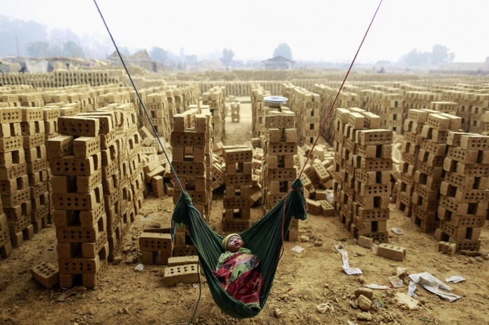 Một bé trai ngủ say trên chiếc võng tại một lò gạch ở ngoại ô thủ đô Yangon của Myanmar, trong khi mẹ em đang làm việc. 