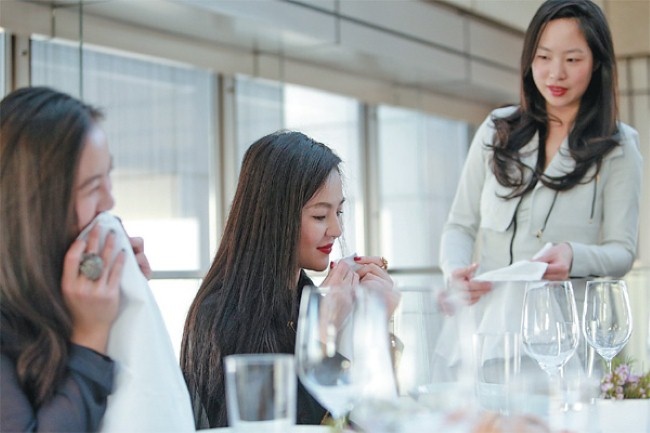 Ho (phải) dạy các học viên giàu có dùng khăn chùi miệng một cách lịch thiệp.