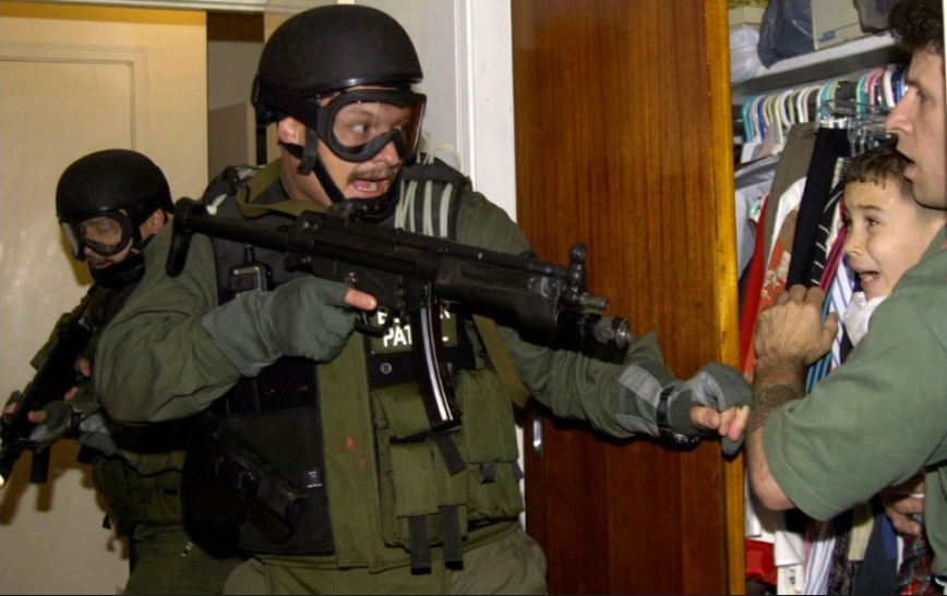 Cảnh một người đàn ông bảo vệ bé Elian Gonalez, 6 tuổi, trước cuộc đột kích của cảnh sát liên bang Mỹ tại Miami, năm 2000. Gonalez đã chứng kiến cảnh mẹ của em chết đuối sau khi thuyền bị cướp khi khởi hành từ Cuba. Theo luật quốc tế, chính quyền Mỹ đã trao trả bé trai về với cha của em tại Cuba. Bức ảnh của Alan Diaz đã giành giải báo chí Pulitzer. 