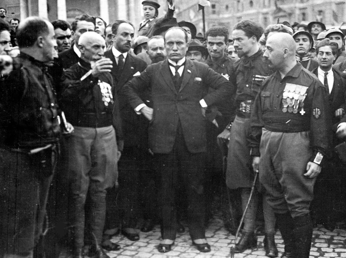 Trùm phát xít Italy Benito Mussolini đứng giữa, tay chống hông, với các thành viên của đảng phát xít, ở Rome, sau một cuộc diễu hành ngày 28/10/1922. Cuộc diễu hành này là một hành động đe dọa. Hàng nghìn phát xít áo đen chiếm vị trí chiến thuật ở khắp Italy. Sau cuộc diễu hành, vua Emanuelle đệ Tam yêu cầu Mussolini xây dựng nên một chính phủ mới, xóa bỏ nền độc tài.