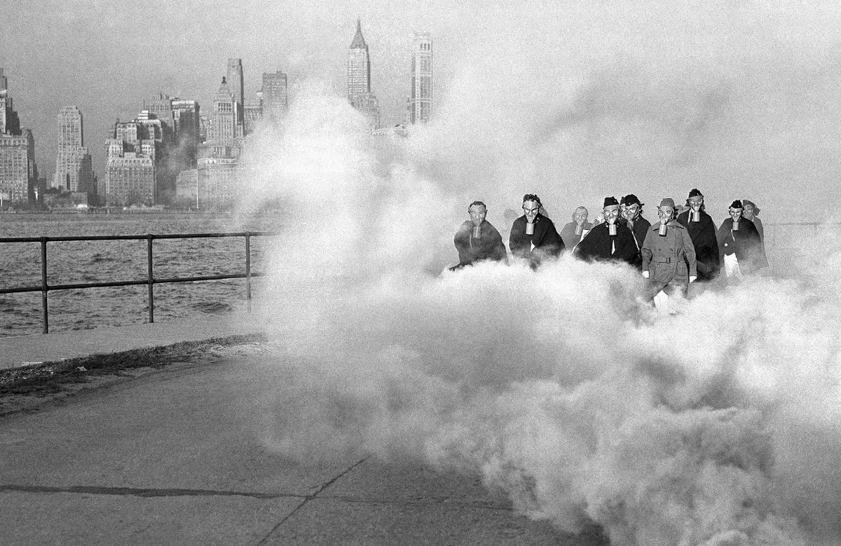 Nhóm nữ quân y của một bệnh viện ở Fort Jay trên đảo Governors, thành phố New York, đeo mặt nạ khí trong buổi diễn tập các biện pháp bảo hộ, ngày 27/11/1941. Phía xa, những tòa nhà chọc trời chìm trong những đám mây khí. 