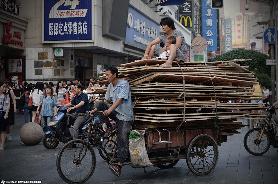 Một người đàn ông chở vợ và con cùng các tấm ván gỗ cồng kềnh trên chiếc xe ba bánh. Họ di chuyển qua con đường đông đúc của thành phố Thượng Hải, Trung Quốc, hôm 1/7.  Ảnh: C