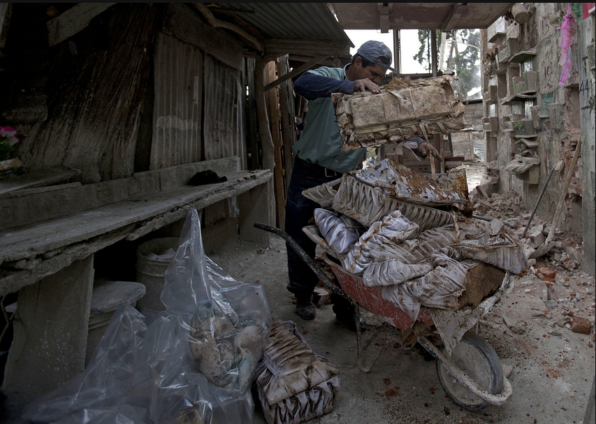 Một công nhân nghĩa trang đặt túi đựng thi hài vừa được khai quật lên xe kéo.