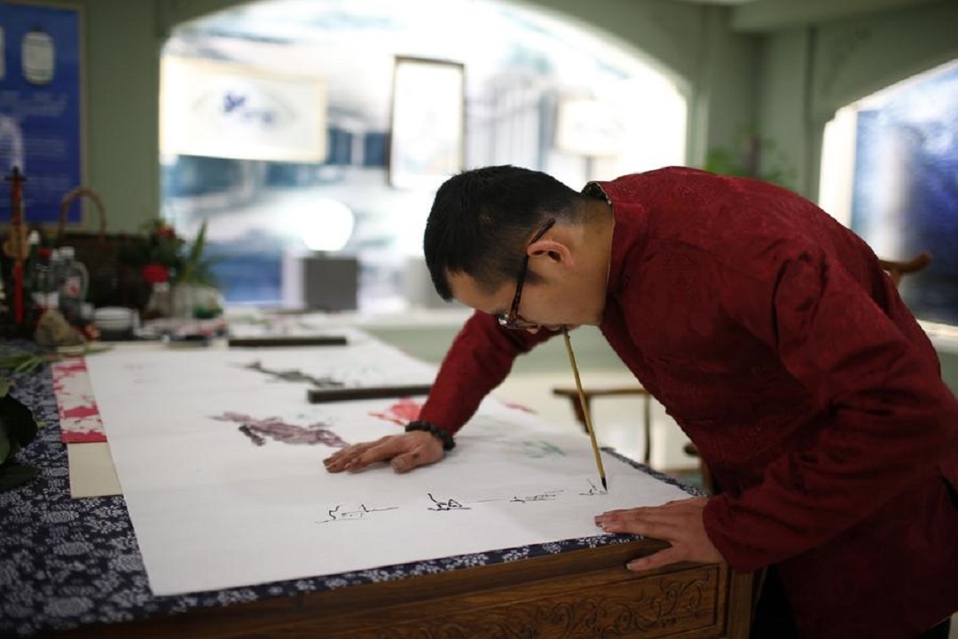 Han Xiaoming ngậm bút lông vào miệng và đề tên lên tác phẩm của anh.