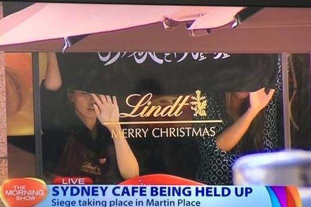 Sydney, Australia ngày 15/12: Các con tin đang bị ép giơ lá cờ màu đen giống của Nhà nước Hồi giáo tự xưng IS. Vụ bắt cóc con tin diễn ra tại quán café Lindt, khu thương mại Martin Palace ở Sydney Australia đang thu hút sự chú ý của thế giới. Truyền thông đưa tin, ít nhất 13 người đang bị giam trong quán café. Kẻ bắt cóc buộc con tin giữ lá cờ màu đen với những dòng chữ tiếng Arab màu trắng trên cửa sổ - dấu hiệu cho thấy rất có thể các tay súng IS đã tới Australia. Nhân viên tại các tòa nhà xung quanh đã được sơ tán. Cảnh sát vũ trang đang bao vây tòa nhà. Ảnh: Independent 