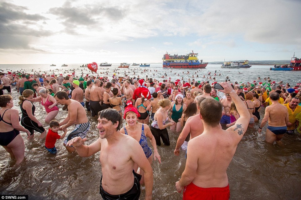 Party: Thousands of Christmas Day swimmers took the plunge in Exmouth, Devon, today for a freezing dip in the sea