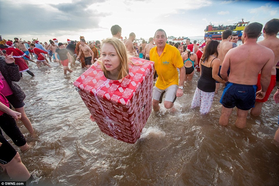 The perfect gift: A girl dressed as a giant Christmas present braves the icy cold water in Devon this morning for the annual swim