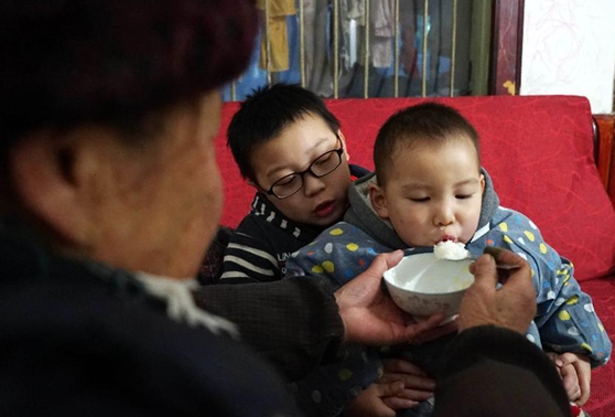 Thiếu niên 10 tuổi giúp bà nội cho em trai ăn. 