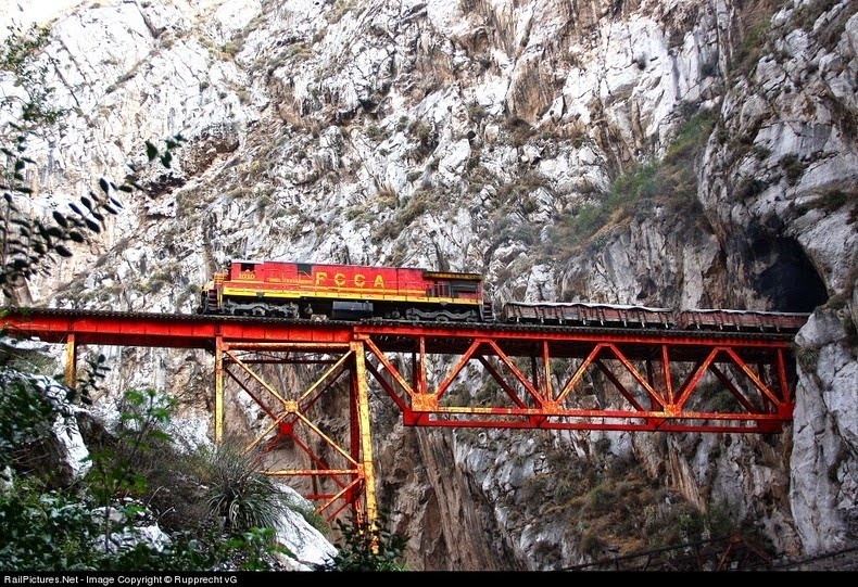 One of the most famous bridges encountered along the Lima to La Oroya line is the Infiernillo or “Little Hell” Bridge, located in a narrow canyon between two tunnels. The track emerges from a tunnel on a vertical cliff, crosses the bridge, and immediately enters another tunnel in a vertical cliff. Underneath the bridge flows the Rio Rimac river, and adjacent to it runs the “Carretera Central” main highway.