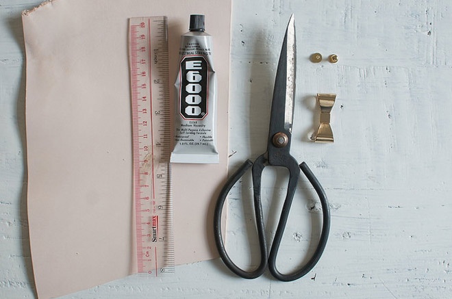 Chuẩn bị đầy đủ nguyên vật liệu gồm 1 chiếc nơ mạ vàng, 1 chiếc nút mạ vàng, 1 cây kéo, 1 cây kềm bấm lỗ, 1 cây thước, miếng vải da màu nude (hoặc màu khác tùy sở thích của bạn) và một ống keo dán.