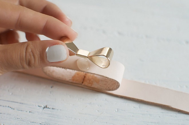 Bước 7: Thoa đều keo lên giữa bề mặt sợi dây da phía trên, sau đó ấn chiếc nơ mạ vàng lên. 