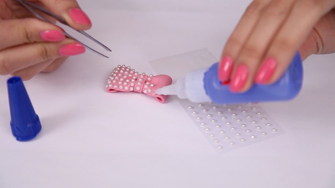 Trang trí chiếc nơ gắn ngọc trai bằng cách dùng keo chấm lên bề mặt nơ, rồi gắn 1 hạt ngọc trai giả vào. Xếp ngọc trai thành đường dài dọc chiều ngang chiếc nơ.