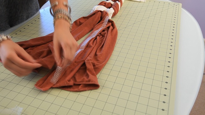 Cắt keo ủi vải thành 1 đoạn bằng chiều dài còn dư của chiếc khăn màu nâu sậm và dán chúng vào 1 cạnh bên của chiếc khăn.