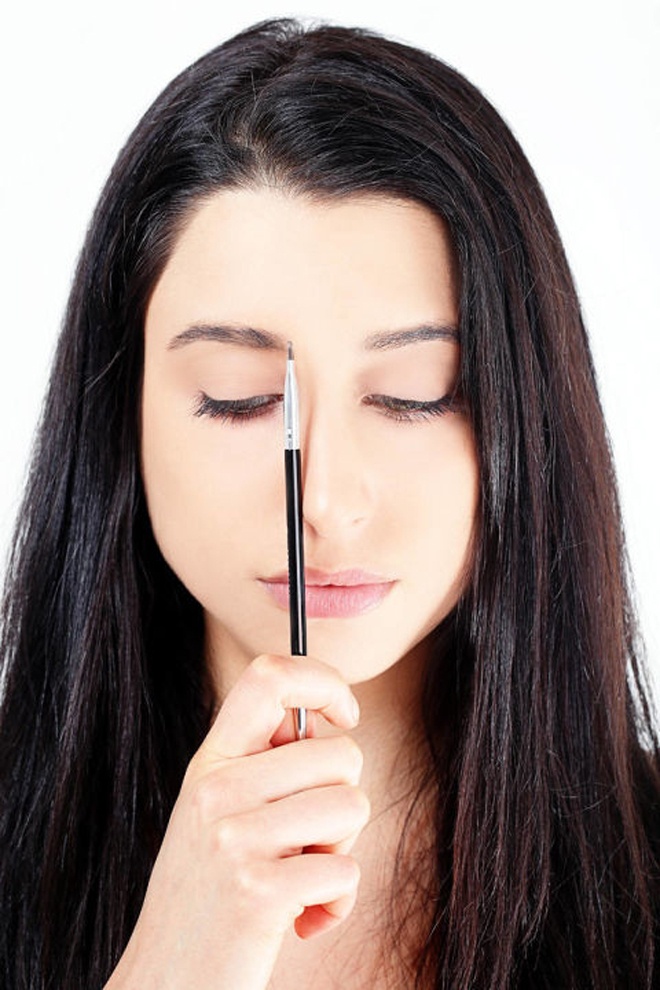 Bước 1. Đầu tiên bạn cần dùng tăm bông thấm nước lau thật sạch lông mày và để khô tự nhiên. Đặt 1 cây cọ trang điểm dọc cánh mũi nhằm xác định chính xác điểm bắt đầu đường vẽ lông mày.