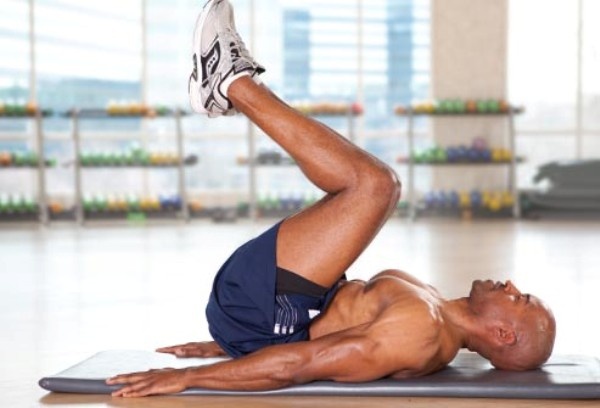 2. The reverse crunch (Gập bụng ngược):  Bước 1: Nằm ngửa trên mặt đất, chân duỗi thẳng, để hai tay song song với cơ thể, lòng bàn tay đặt cố định trên mặt đất.  Bước 2: Nâng chân lên cho tới khi đùi vuông góc với mặt đất và hai bàn chân sát vào nhau để song song với mặt đất. Bước 3: Trở lại vị trí ban đầu, nhưng không để chân chạm xuống đất. Điều này giúp duy trì sự căng cơ bụng trong suốt quá trình tập luyện. Lặp lại động tác này 12 lần. Ảnh: Webmd.