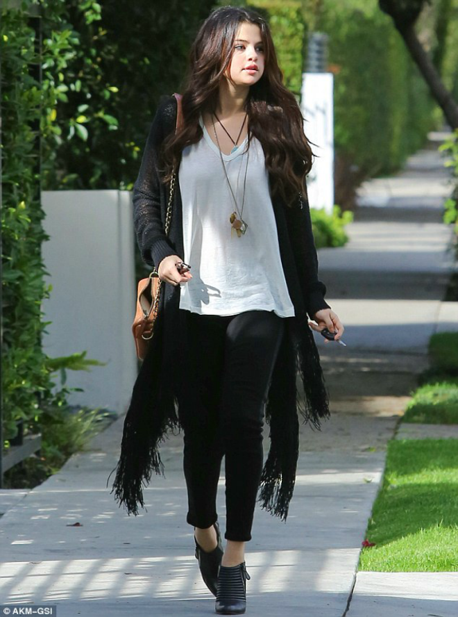 Selena Gomez cực kỳ năng động, cá tính với cardigan tua rua tông màu đen, áo thun trắng, quần skinny và bốt cổ thấp.