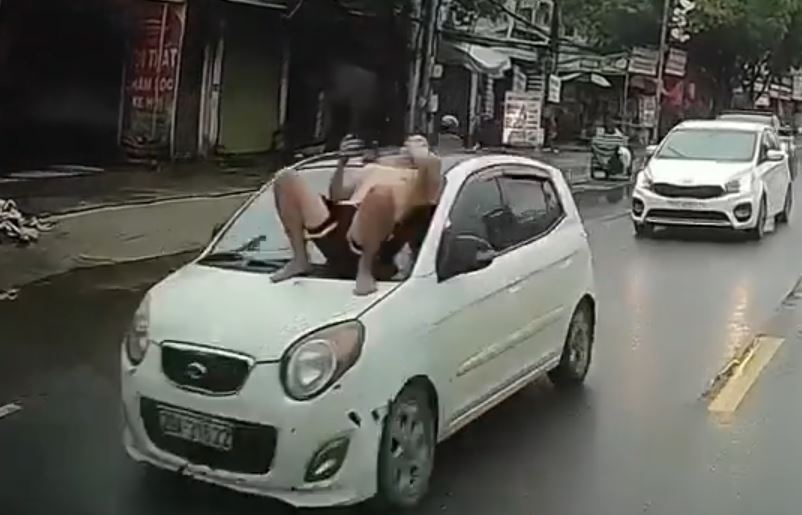 Nguoi dan ong nam tren capo o to dang chay giua pho Ha Noi hinh anh