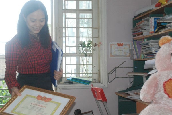 Tay phải cầm tấm bằng khen chống tiêu cực, tai trái chị 