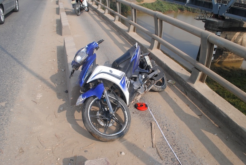 Sau cú va chạm với thành cầu cực mạnh, chiếc xe Exciter nằm vắt ngang ven lề đường. Đôi nam nữ bị văng xa nhiều mét. Ảnh: Duy Cảnh.