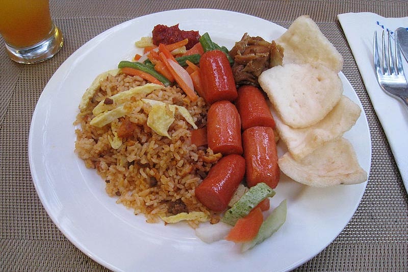 4. Nasi Goreng. Nasi Goreng bao gồm cơm chiên ăn kèm với các món ăn phụ khác như rau, nước sốt… Món Nasi Goreng đặc biệt còn được chiên cùng me và ớt, thêm trứng và tôm. Du khách có thể thưởng thức món Nasi goreng cùng rau bắp cải, xúc xích và món thịt truyền thống của Indonesia.