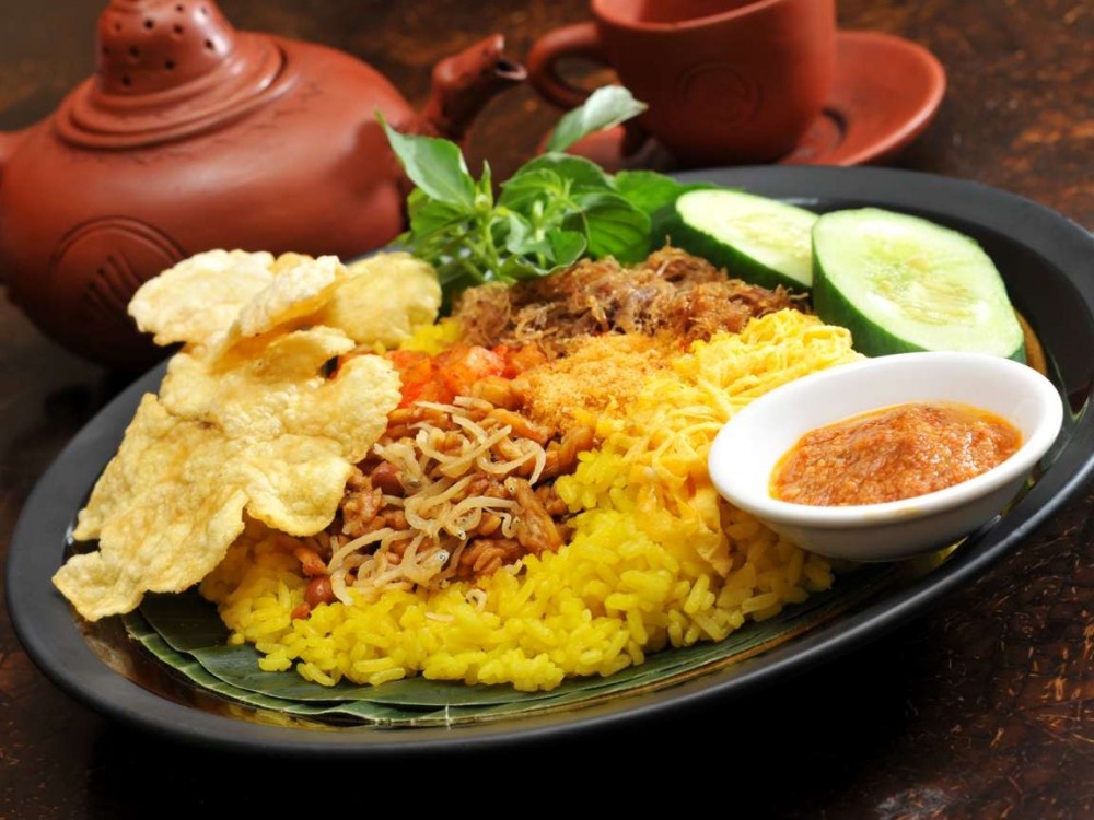 5. Nasi Kuning. Nasi Kuning là món ăn được làm từ một loại gạo vàng đặc biệt thường được người dân Bali dùng trong các dịp lễ hội, cúng tế. Gạo được nấu với nước cốt dừa cùng với nước hầm gà, thêm những gia vị thơm và một bí quyết nấu khéo léo sao cho những hạt cơm khi chín rời nhau từng hạt riêng biệt. Nasi Kuning thường được dọn ra trên đĩa lớn và trang trí rất đẹp mắt, ăn kèm với trứng, thịt, cá…rất ngon miệng.