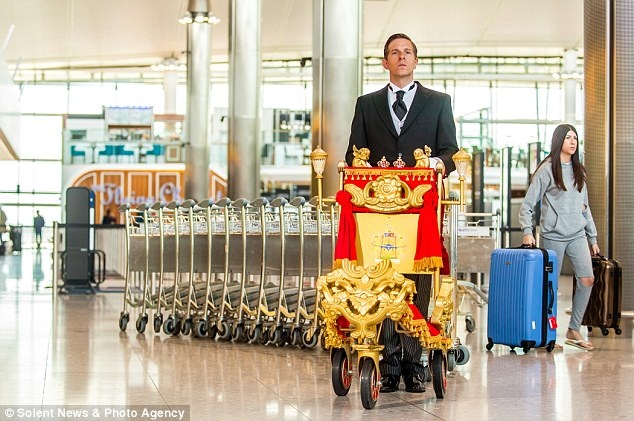 Chiếc xe đẩy kỳ lạ được trang trí bằng nhung đỏ và dải tua viền vàng theo phong cách hoàng gia Anh được điều khiển bởi một người đàn ông ăn mặc trang trọng  thu hút sự chú ý của những du khách có mặt ở sân bay.