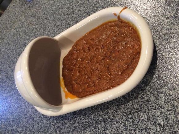 Ban đầu, món ăn được chế biến cho một bộ phim của Shimizu với cảnh quay anh phải ăn thứ chất thải bốc mùi. Sau đó, Shimizu quyết định biến nó trở thành món ăn chủ đạo cho nhà hàng Curry Shop Shimizu anh mới mở. Món cà ri táo bạo này được làm từ trà xanh, bitter gourd và bột ca cao, được đựng trong những chiếc bát hình bồn cầu. Bột ca cao trộn nước thành hỗn hợp nhão rất dễ liên tưởng đến thứ nhạy cảm của con người.