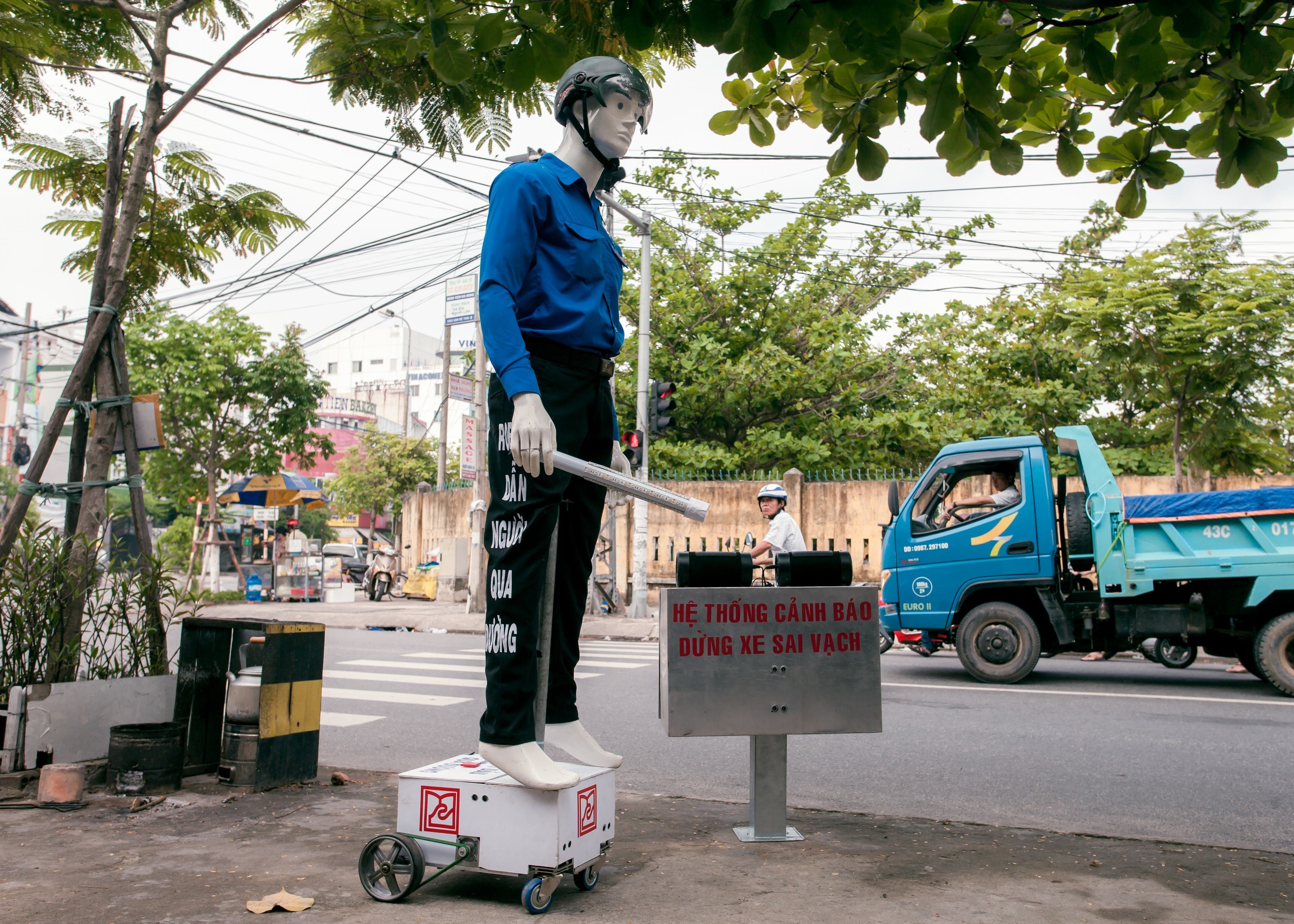 robot cao 1,9m, đội mũ bảo hiểm, tay phải cầm gậy có gắn hệ thống đèn, tay trái dẫn khách qua đường, trên miệng có còi hú để xin người tham gia giao thông nhường đường. 