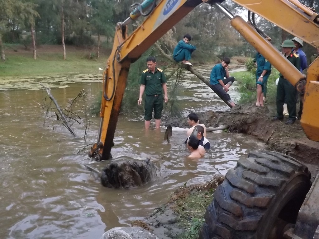Dùng máy cẩu và sức người trục vớt quả bom lên bờ.