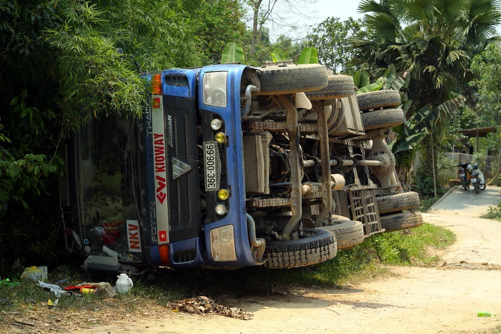 Chiếc xe tải bị lật nghiêng bên đường, ngay ở mép bờ ao.