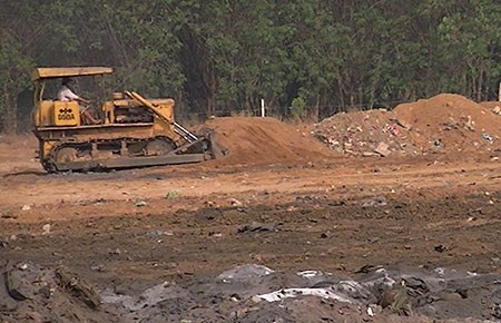 Xe ủi đang đưa đất lấp các hố chôn chất thải. 