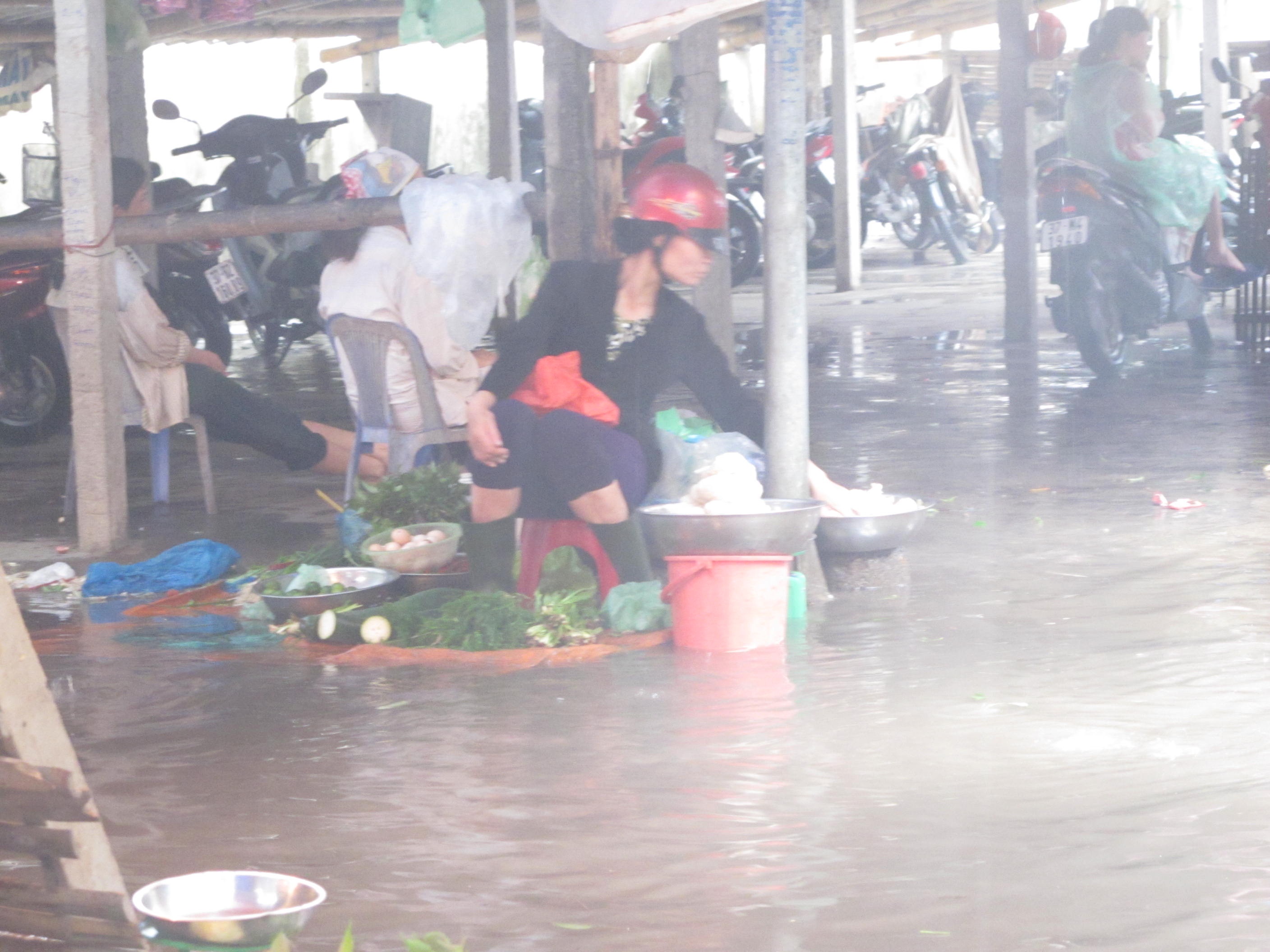 Người phụ nữ ngồi bán hàng giữa biển nước mênh mông. Chị cho biết quê ở huyện Hưng Nguyên. Lúc sáng lên thành phố Vinh bán hàng chị không nghĩ chợ lại bị ngập nặng như vậy.