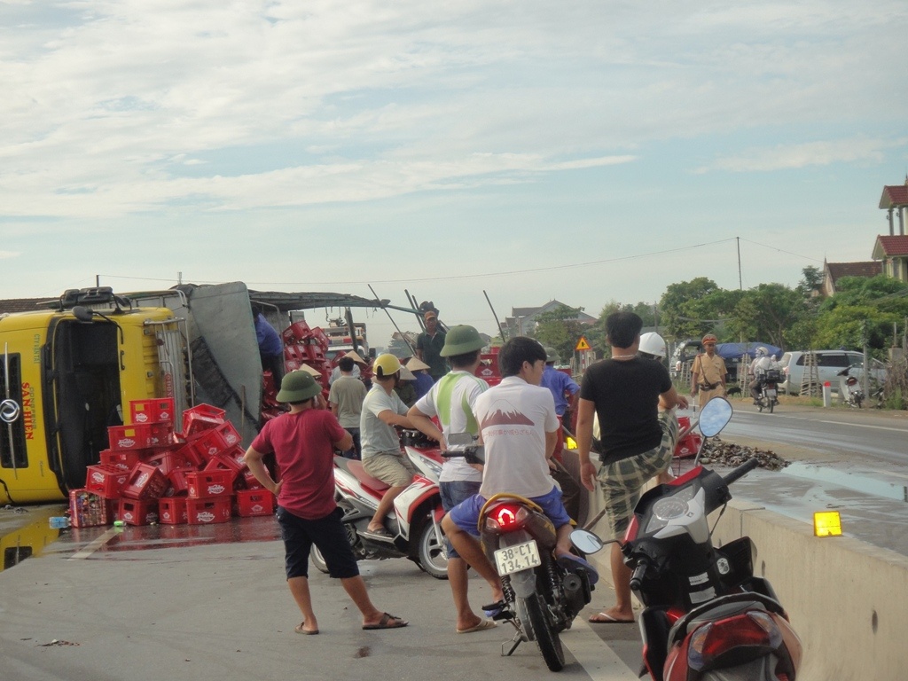 Vụ tai nạn khiến hàng trăm thùng bia từ trên thùng xe rơi ra đường, bắn tung tóe khắp nơi. Nhiều chai bia bị vỡ nát. 