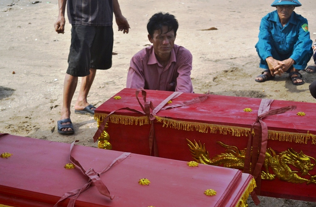 Anh Vũ Văn Đường (áo đỏ) ngồi bệt xuống đất, lặng nhìn quan tài hai con trai. Ảnh: N.Dương